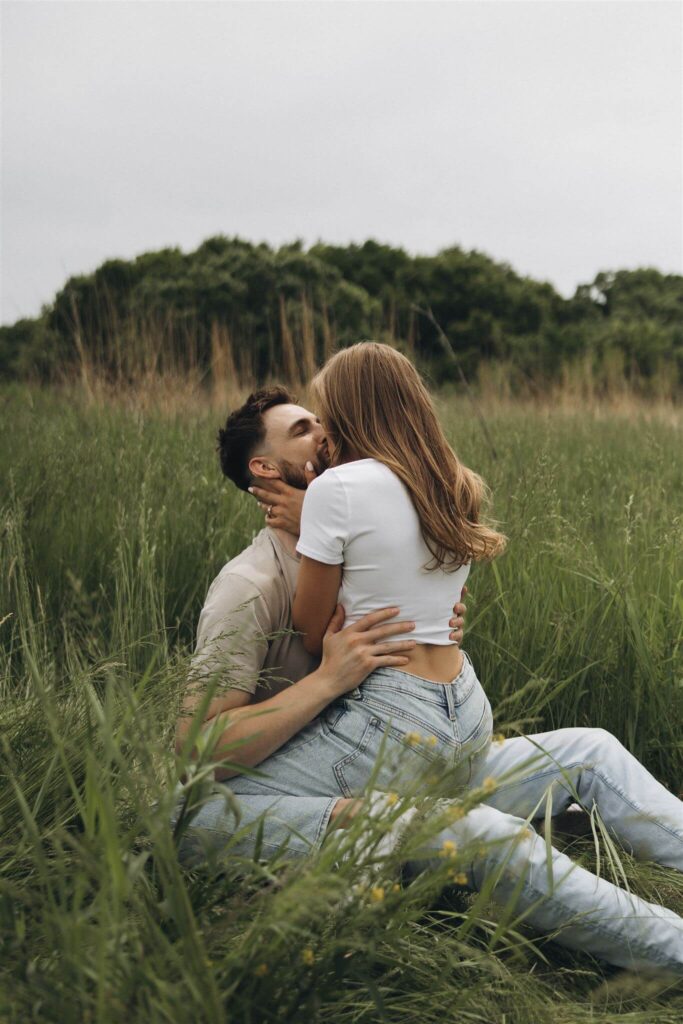 Woman sits on man's lap and kisses him while holding both sides of his face