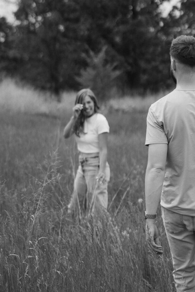 Woman in white tee and denim jeans looks back at her fiancee as he walks towards her