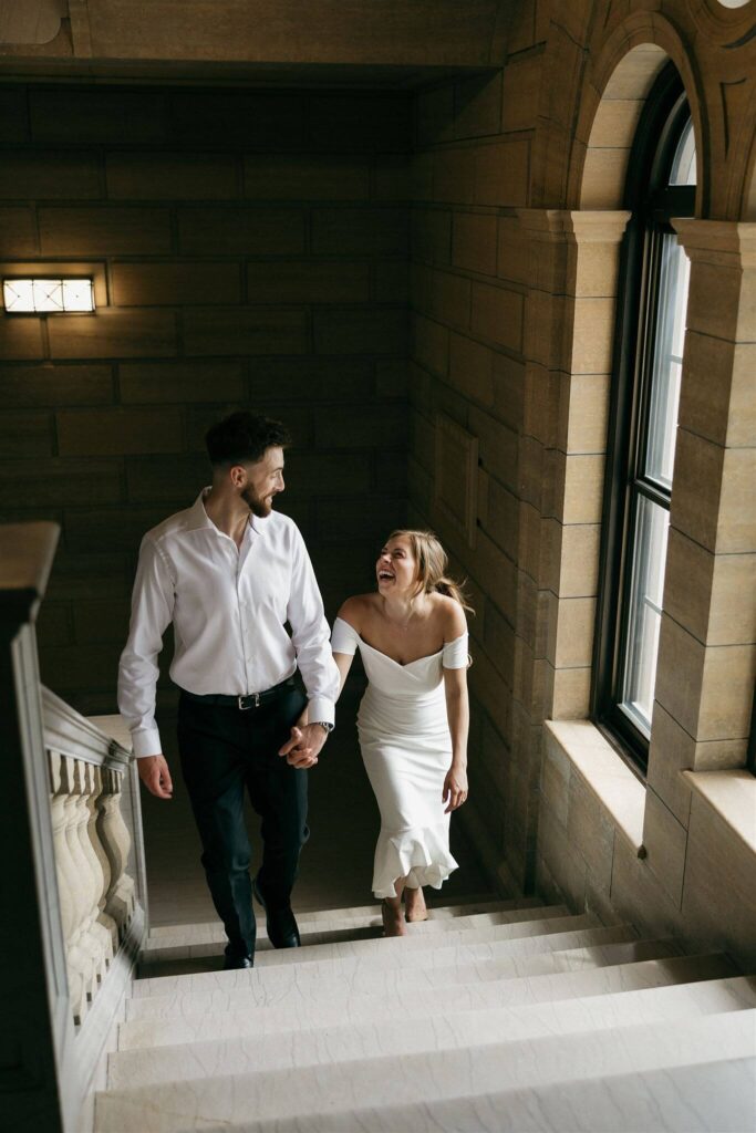 Engaged couple laughs while walking up elegant Minnesota stairwell in engagement photos