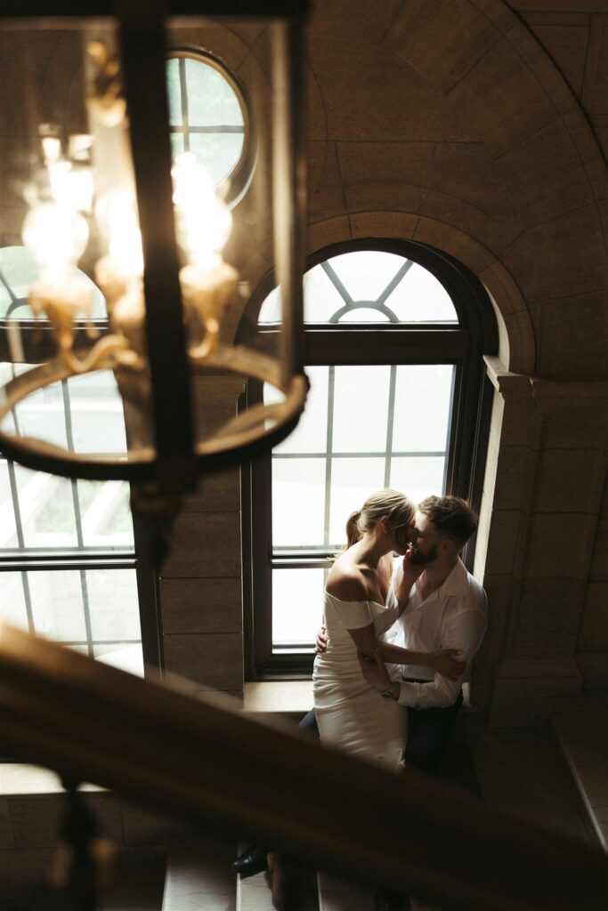 Man and woman go in for a sensual kiss in the dark stairwell of an elegant building