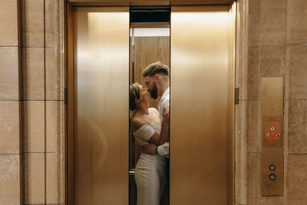 Man and woman kiss in elevator with golden doors