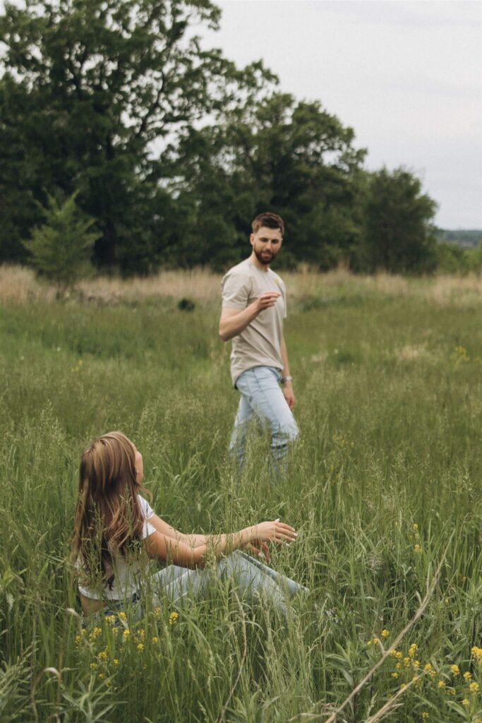 Woman sitting in the grass laughs as man picks her a flower