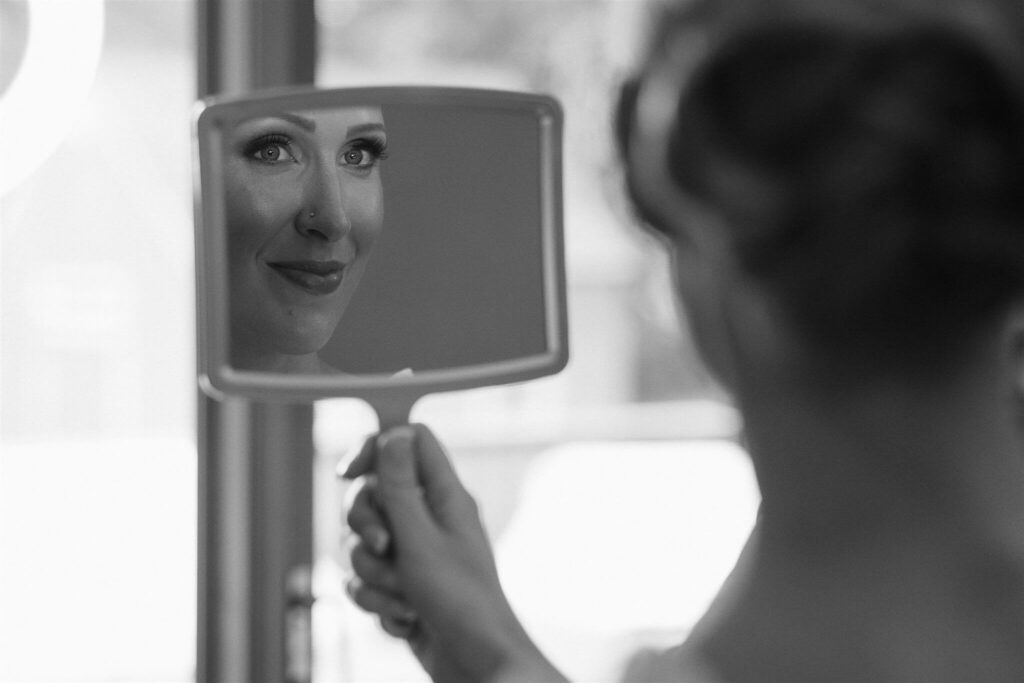 Bride smiles at her reflection in handheld mirror