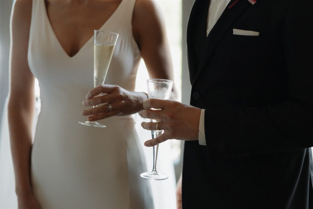 Bride and groom hold champagne flutes in microwedding cocktail hour