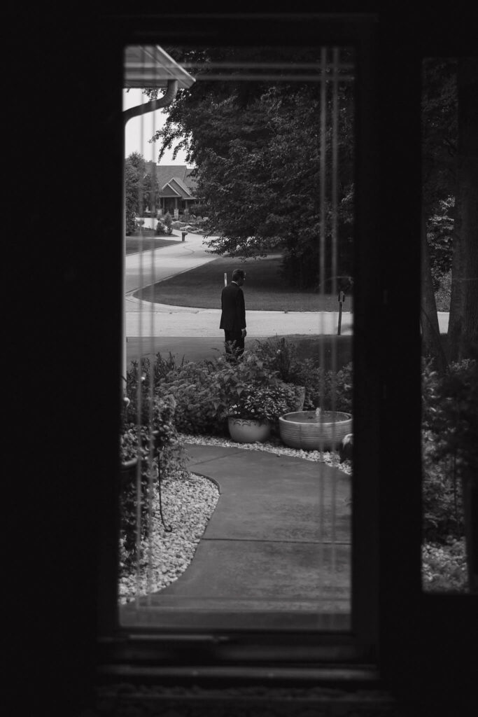 Father of the bride patiently waits in the drive for first look with his daughter