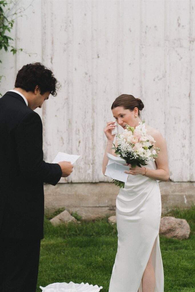 Bride wipes her eyes with a handkerchief as groom reads his wedding vows to her