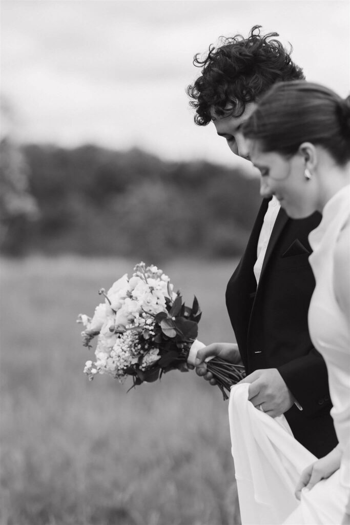 Groom holds bride's bouquet as they walk through Minnesota meadow