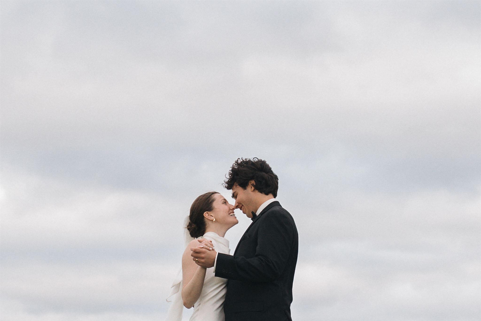 Bride and groom embrace under an overcast sky