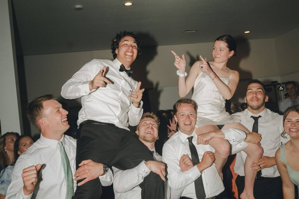 Bride and groom sit on groomsmen's shoulders