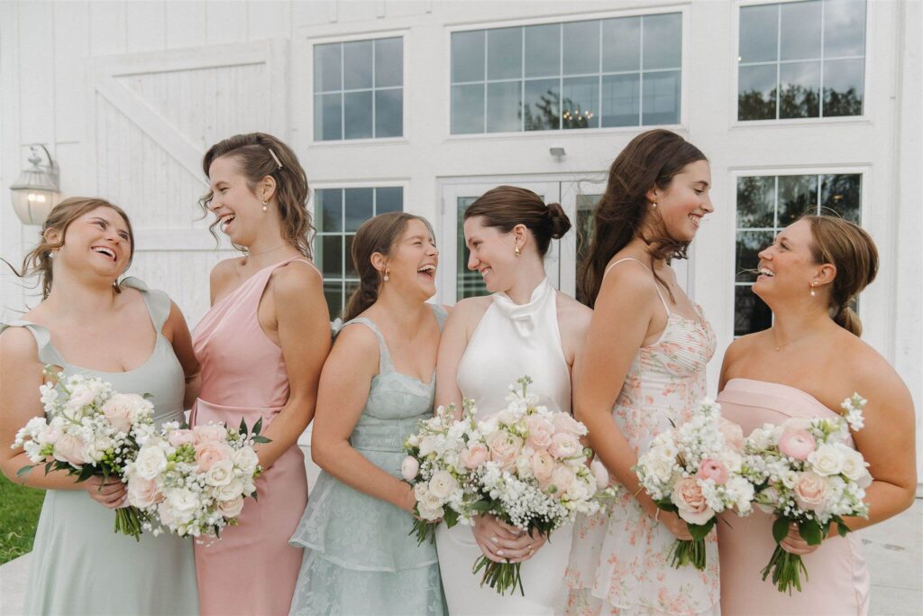 Bride laughs with her bridesmaids dressed in pastel-colored gowns