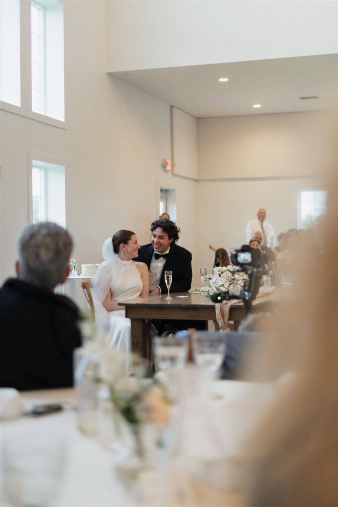 Groom smiles at his wife as they listen to the wedding speeches