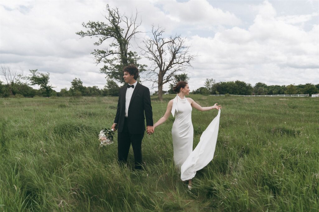 Bride and groom walk through meadow on overcast wedding day