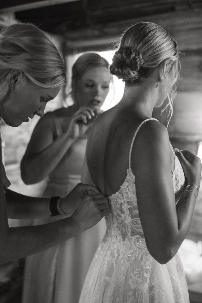 Bride's sisters button up her wedding gown at farm wedding venue