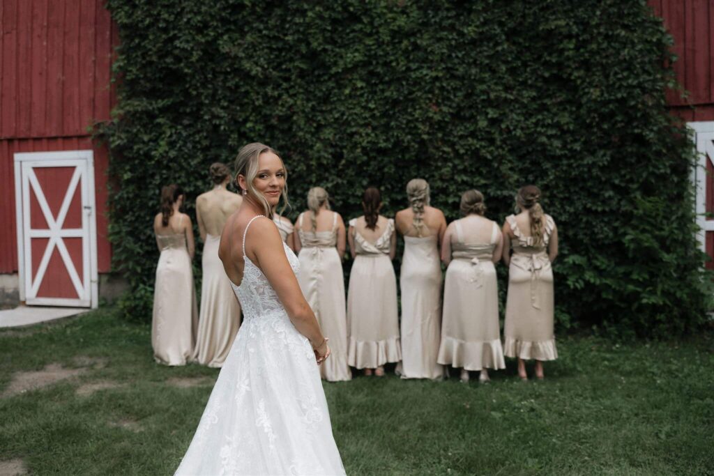 Bride smiles over her shoulder before the first look with her bridesmaids at Minnesota farm wedding venue