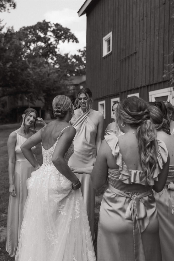 Bride and her bridesmaids laugh and talk outside barn