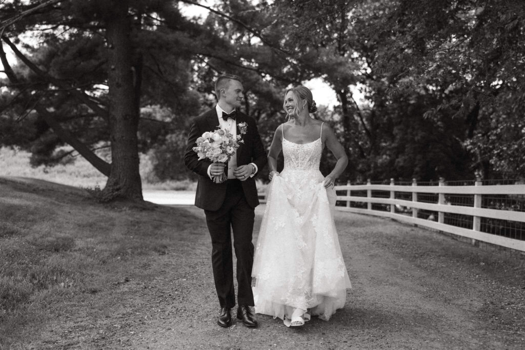 Bride and groom walk on gravel road lined by a white fence at Hope Glen Farm wedding venue in Minnesota