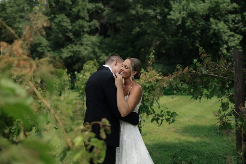 Bride grins as her groom kisses her neck