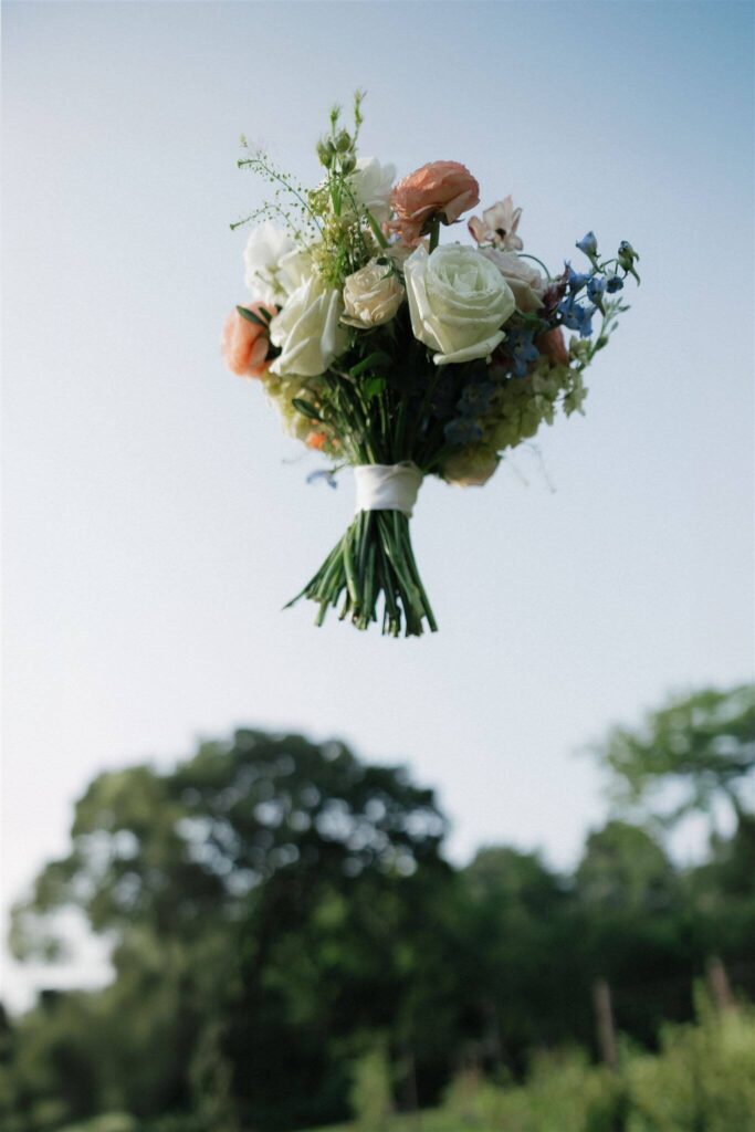 Bride's bouquet is tossed in the air at farm wedding venue