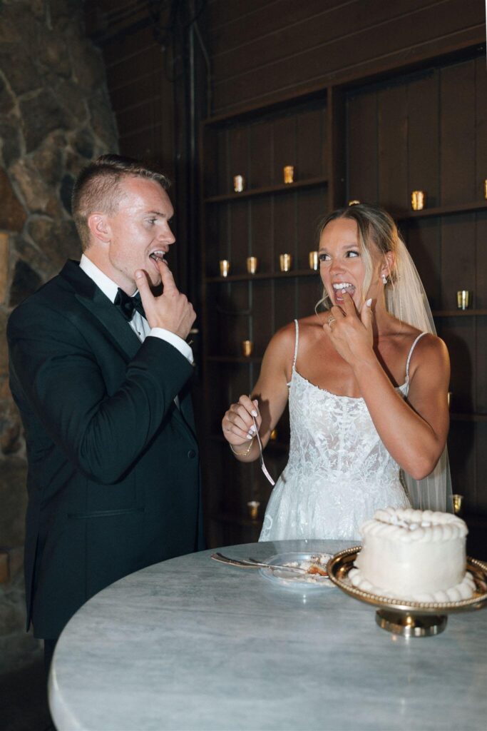 Bride and groom lick their fingers and look at each other after tasting their wedding cake