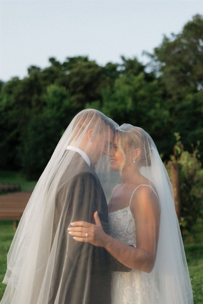 Bride and groom touch foreheads underneath the bride's veil during golden hour