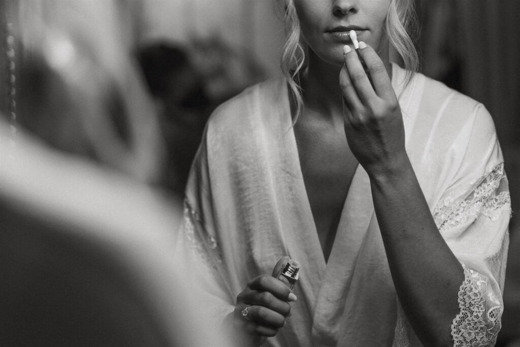 Bride applies lip gloss while wearing a satin robe