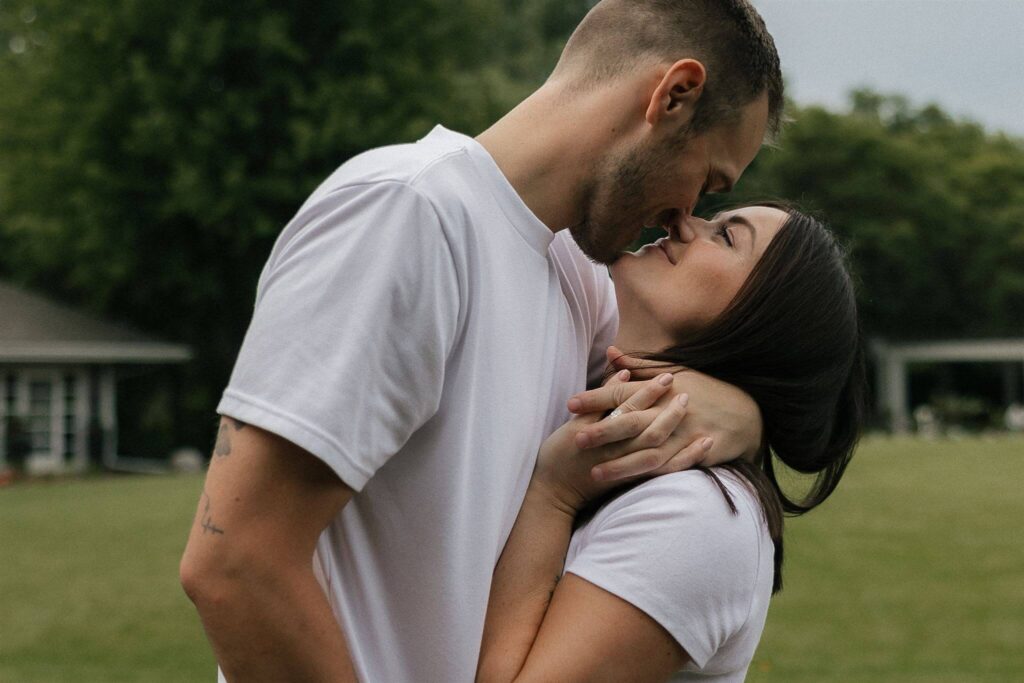 Man leans in to kiss his fiance with his hand intertwined with hers