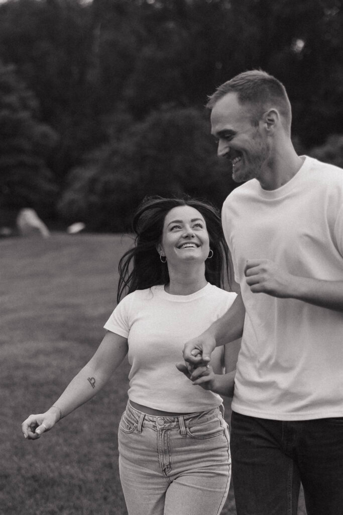 Engaged couple runs through park hand in hand