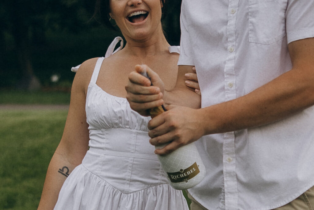 Engaged couple uncork champagne to celebrate their engagement photo shoot