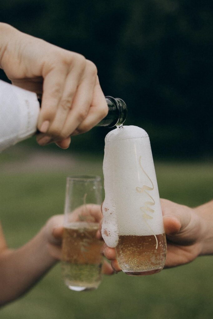 Engaged couple holds champagne glasses while pouring celebratory champagne