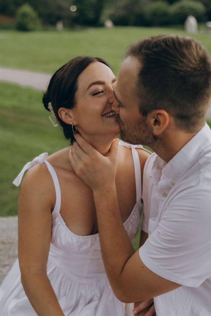 Woman smiles as her fiance leans in to kiss her during engagement photo shoot