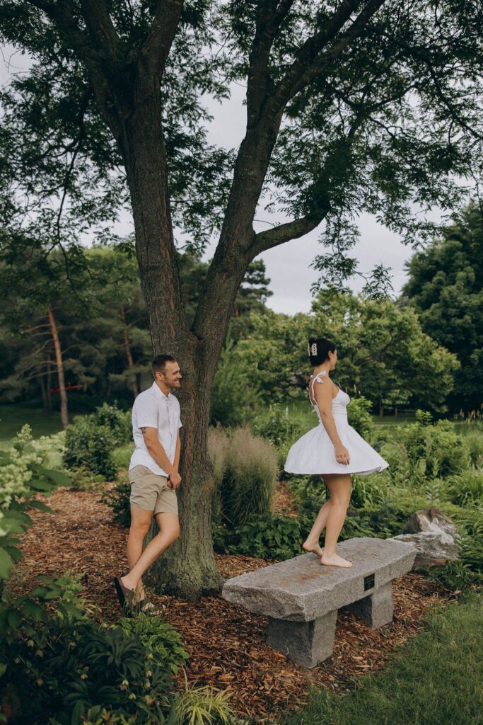 Man looks on happily as his fiance twirls around on a park dress while wearing a white dress