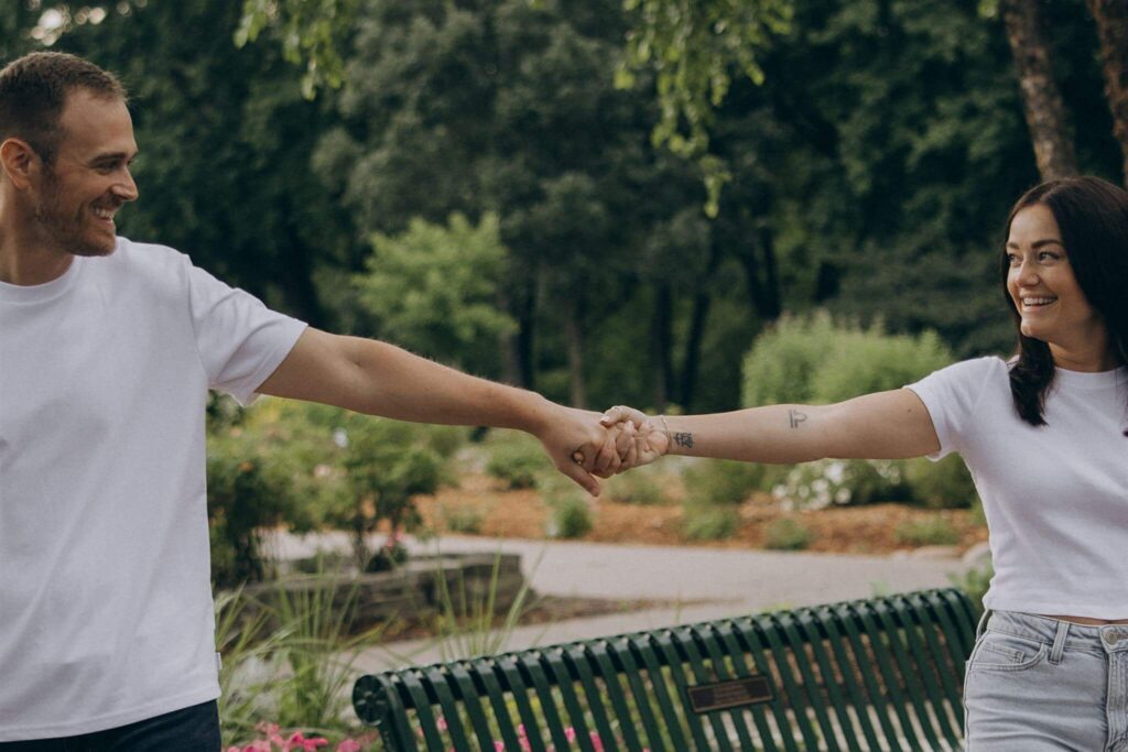 Engaged couple stands far apart with hands outstretched in park engagement photo shoot 