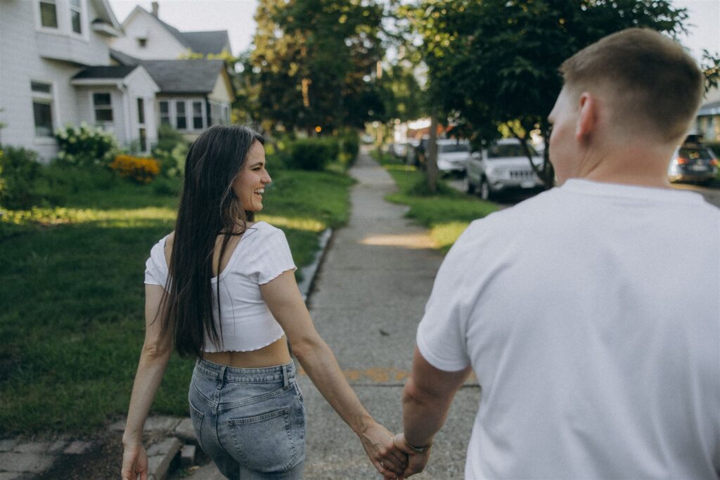 Engaged couple walks hand in hand down their neighborhood sidewalk