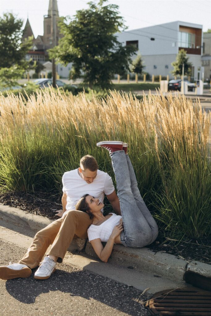 Woman sticks her Converse-clad feet up in the air while her head rests in fiance's lap