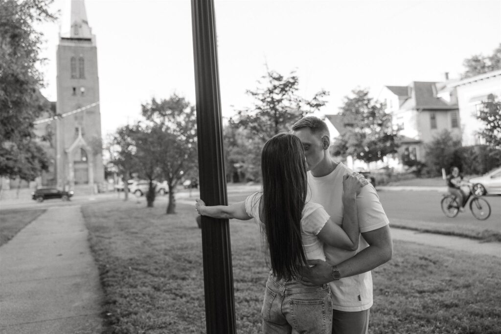 Woman holds onto lamppost as her fiance kisses her in Minneapolis street for engagement photography ideas