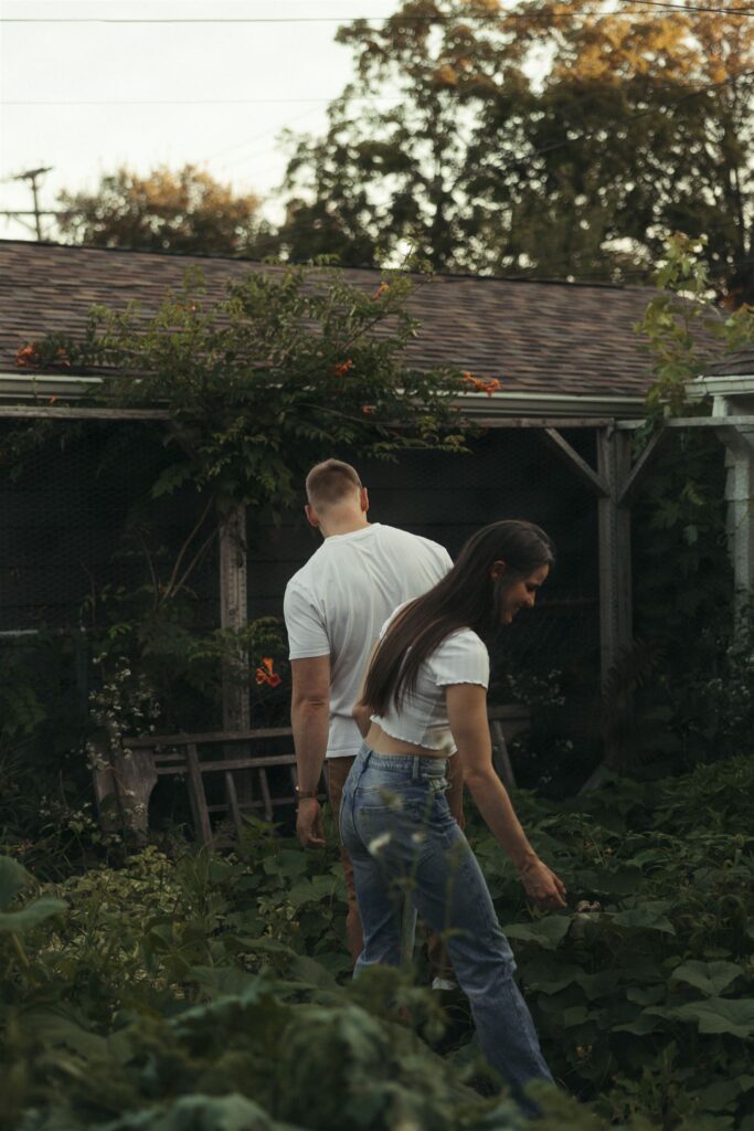 Engaged couple wanders through their overgrown garden in their Minneapolis backyard