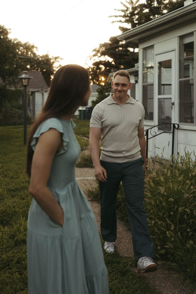 Woman wearing blue dress smiles back at her fiance as he walks towards her 