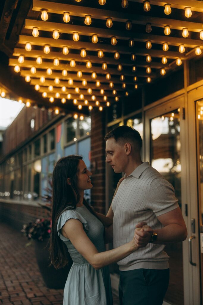 Man looks down at woman as they practice their first dance under marquee lights