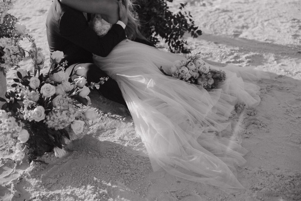 Bride and groom sit in the sand on the beach at destination elopement