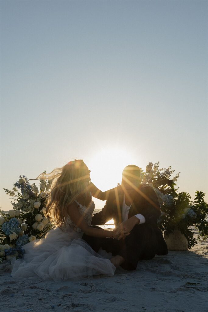 Newlyweds sit in the sand as the sun fades into the horizon 