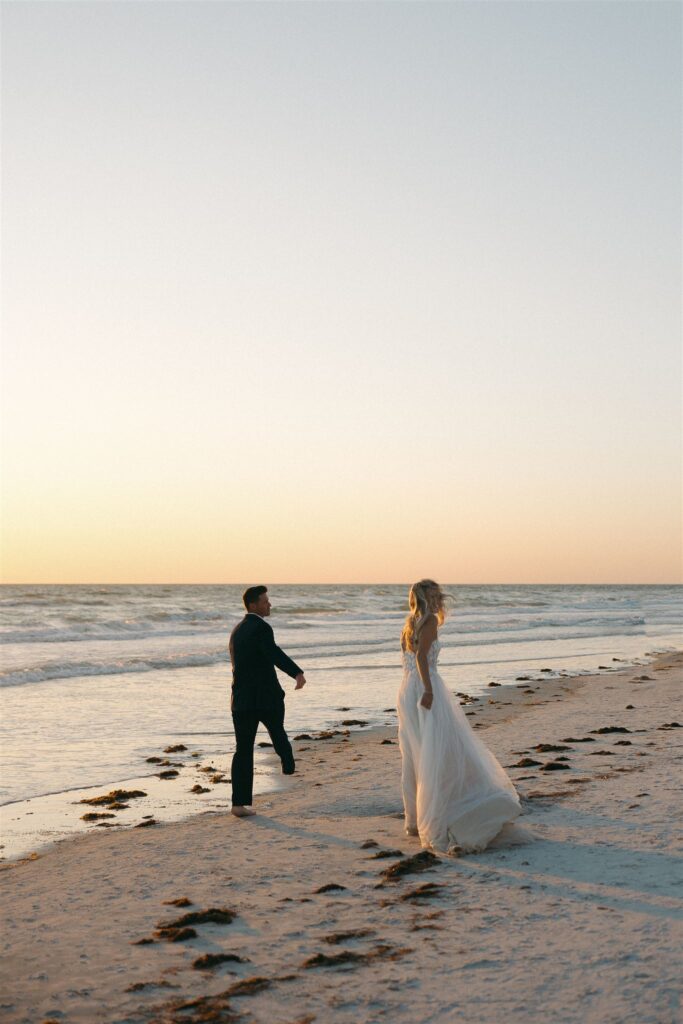 Newlyweds walk along the beach as waves hit the shore