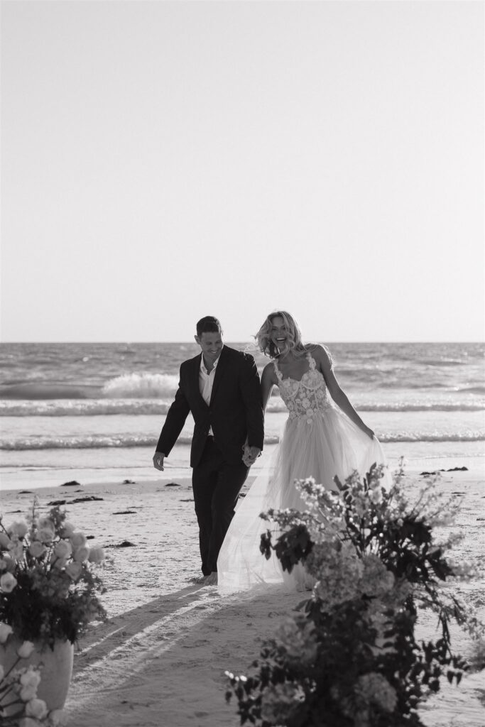 Bride and groom walk hand in hand in the sand