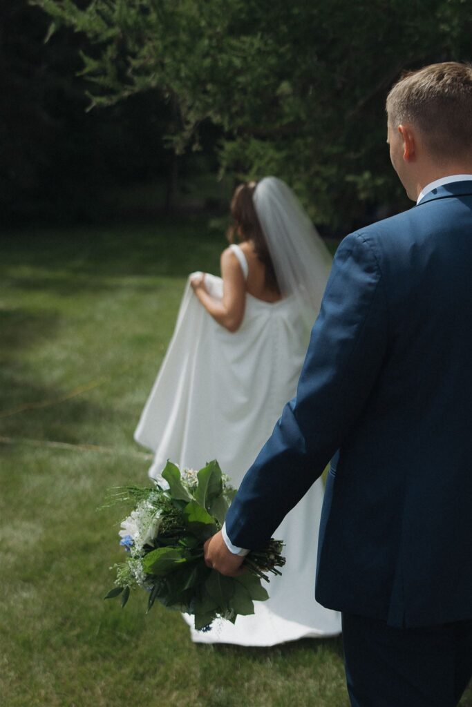 Groom walks behind bride while holding her bouquet