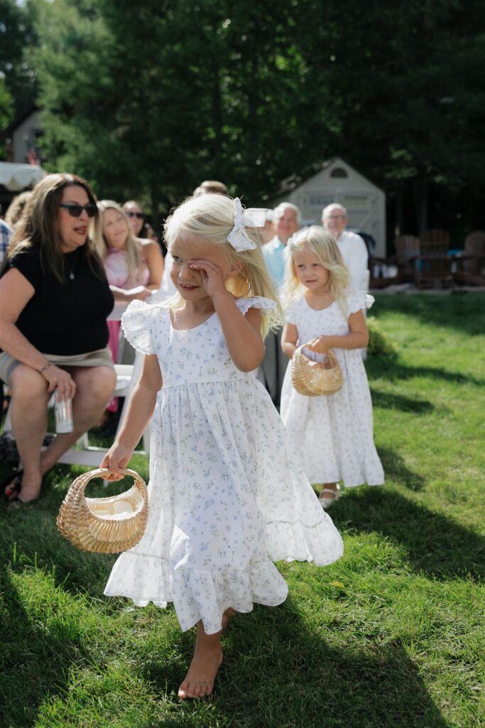 Flower girl smiles and wipes her sleepy eyes as she comes up the aisle