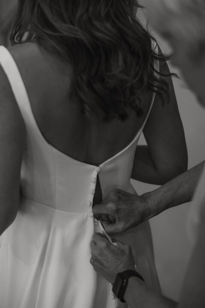 Mother of the bride buttons up the bride's dress