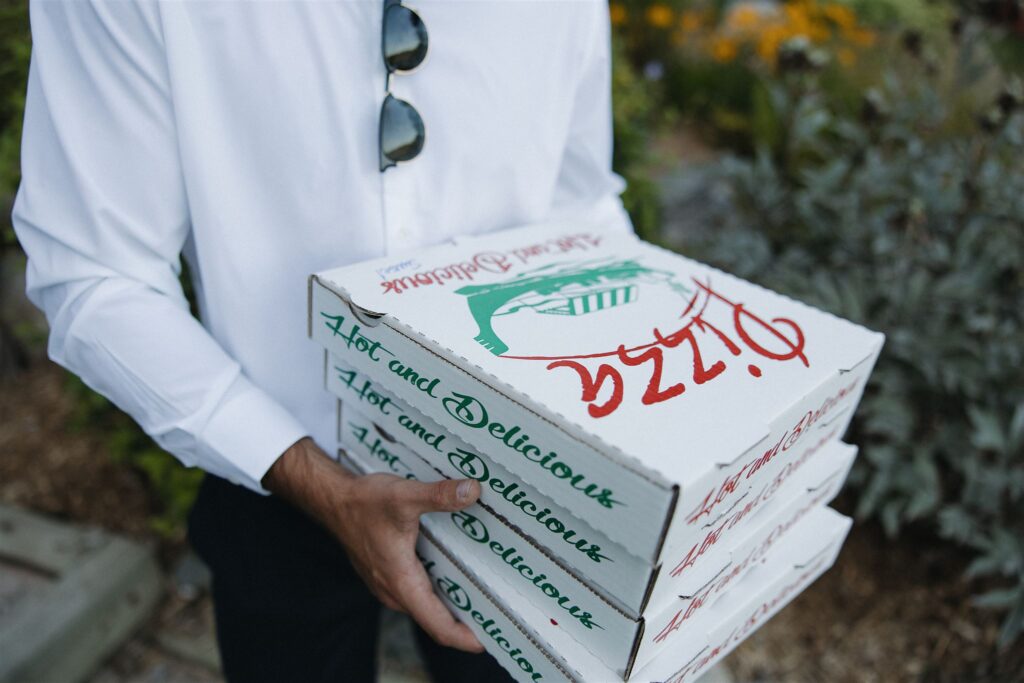 Groomsman holds four boxes of pizza for the wedding reception