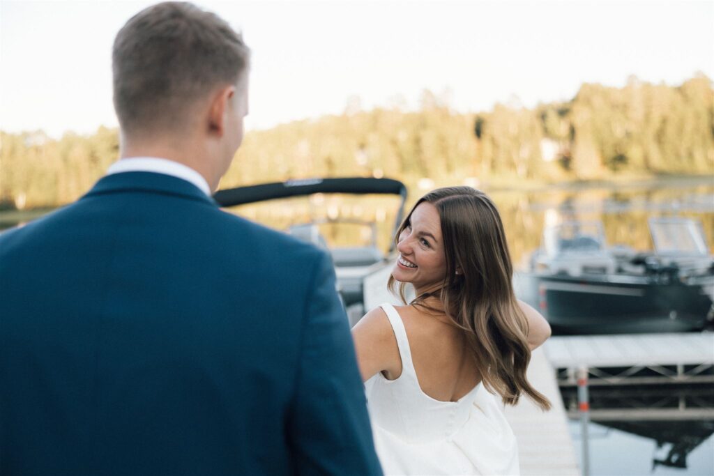 Bride grins back at groom as they walk towards their boat for a sunset cruise on Lake Leech in Walker, Minnesota