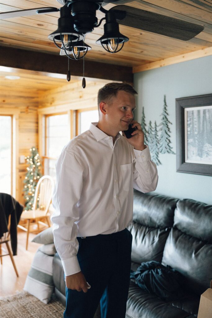 Groom stands in the living room of his cabin in Walker, Minnesota while talking to someone on the phone