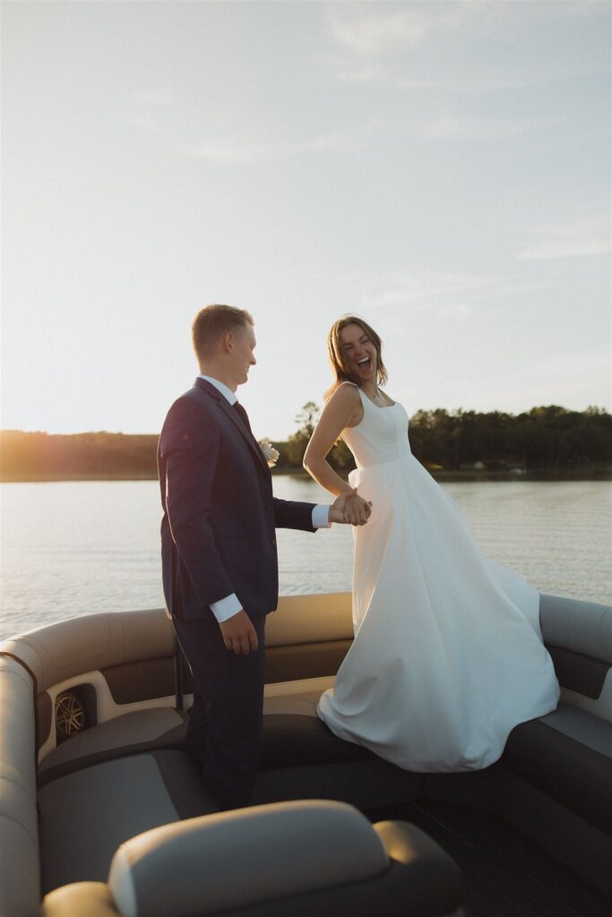 Groom holds bride's hand as she dances on the bench seat of the boat