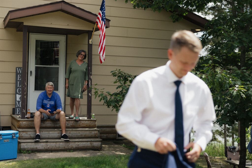 The parents of the groom watch him head to the ceremony space from the steps of their front porch